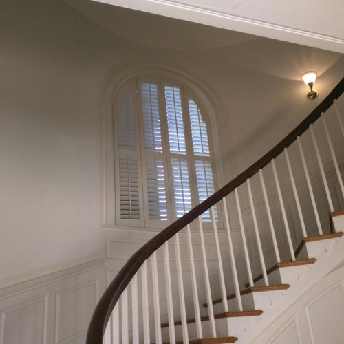 White plantation shutters decorating rounded window located in spiral stairwell.